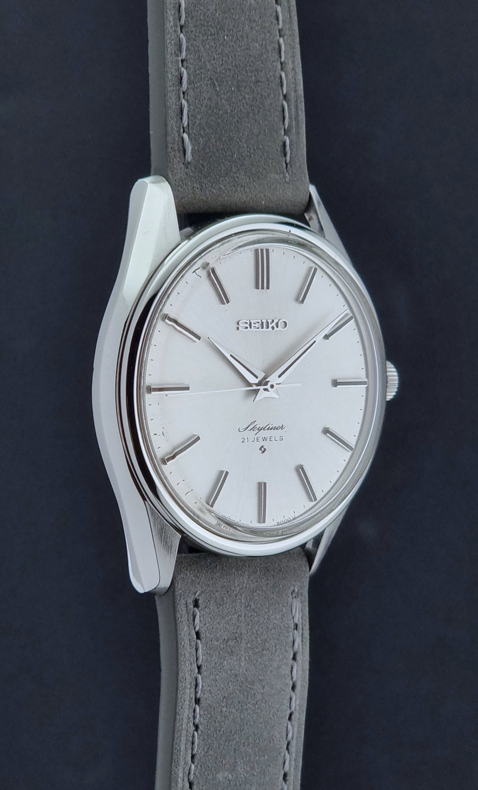 Vintage Seiko Wristwatch Skyliner 6100-8000 with a grey leather strap and silver case on a grey background side profile view