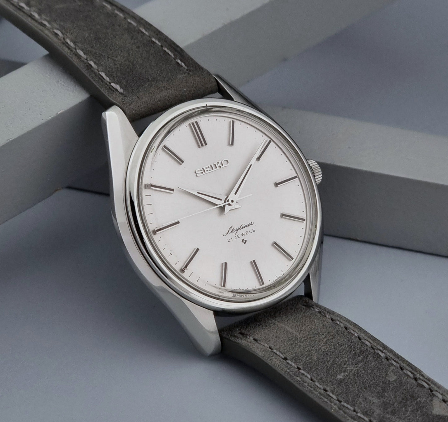 Vintage Seiko Wristwatch Skyliner 6100-8000 with a grey leather strap and silver case on a grey background side view