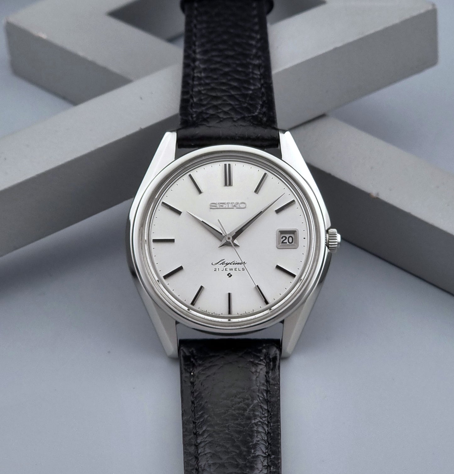 Vintage Seiko Wristwatch Skyliner 6102-8000 with black leather strap and silver case on a light gray background dial view