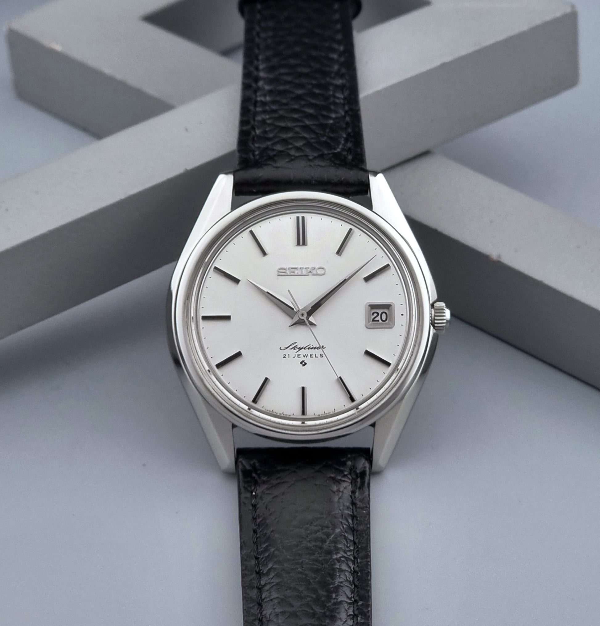 Vintage Seiko Wristwatch Skyliner 6102-8000 with black leather strap and silver case on a light gray background dial view