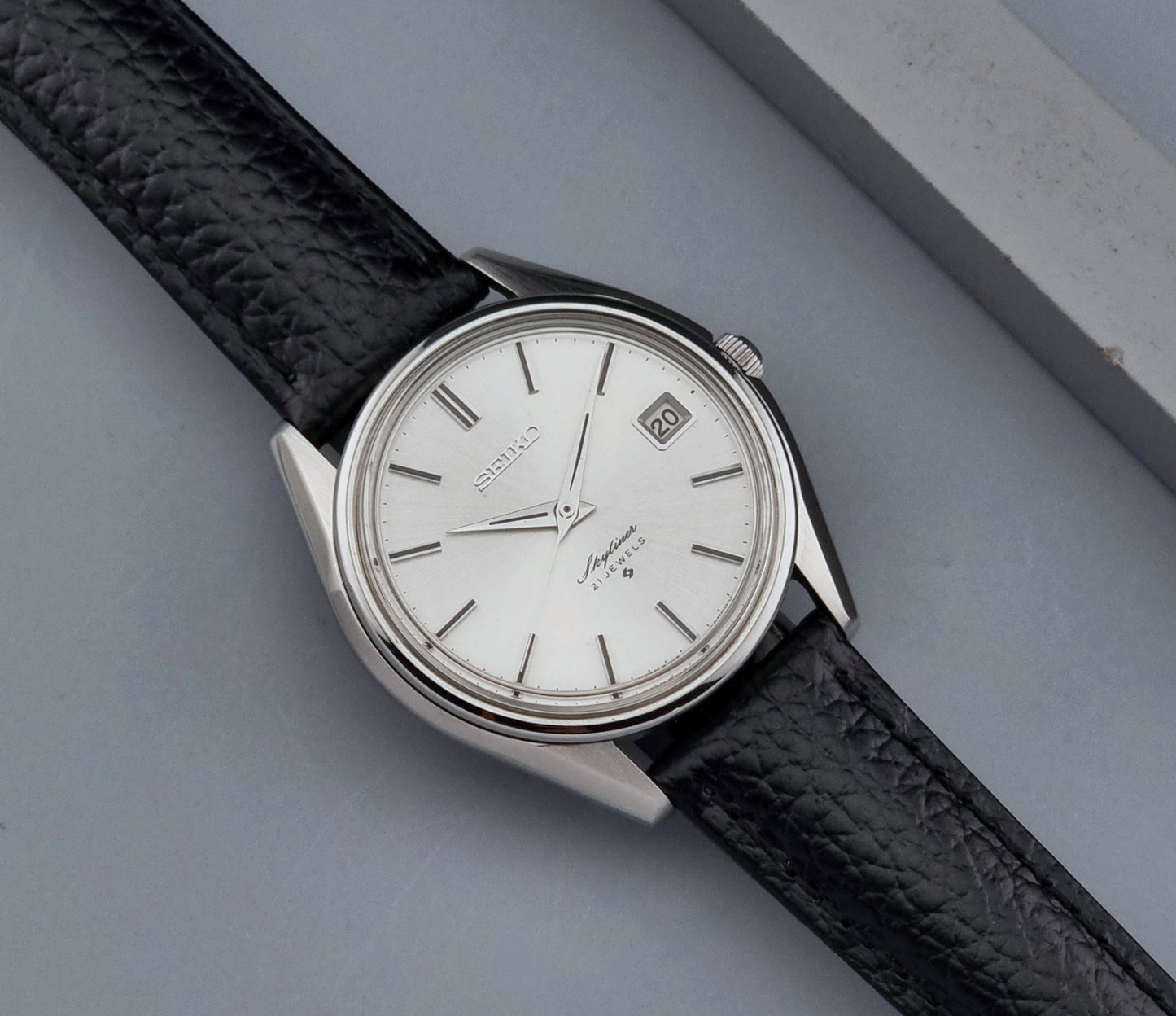 Vintage Seiko Wristwatch Skyliner 6102-8000 with black leather strap and silver case on a light gray background close up dial view