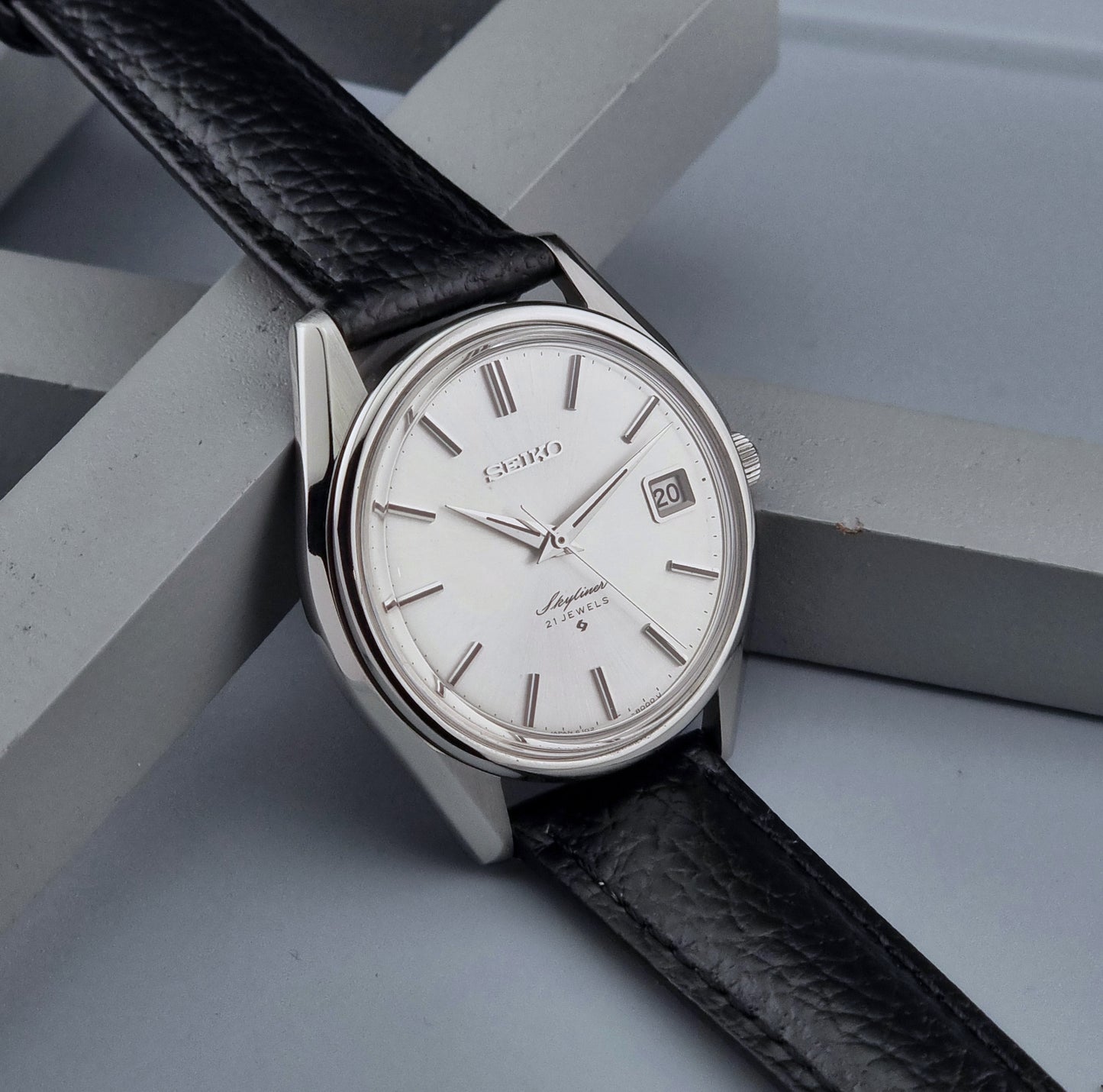Vintage Seiko Wristwatch Skyliner 6102-8000 with black leather strap and silver case on a light gray background side view