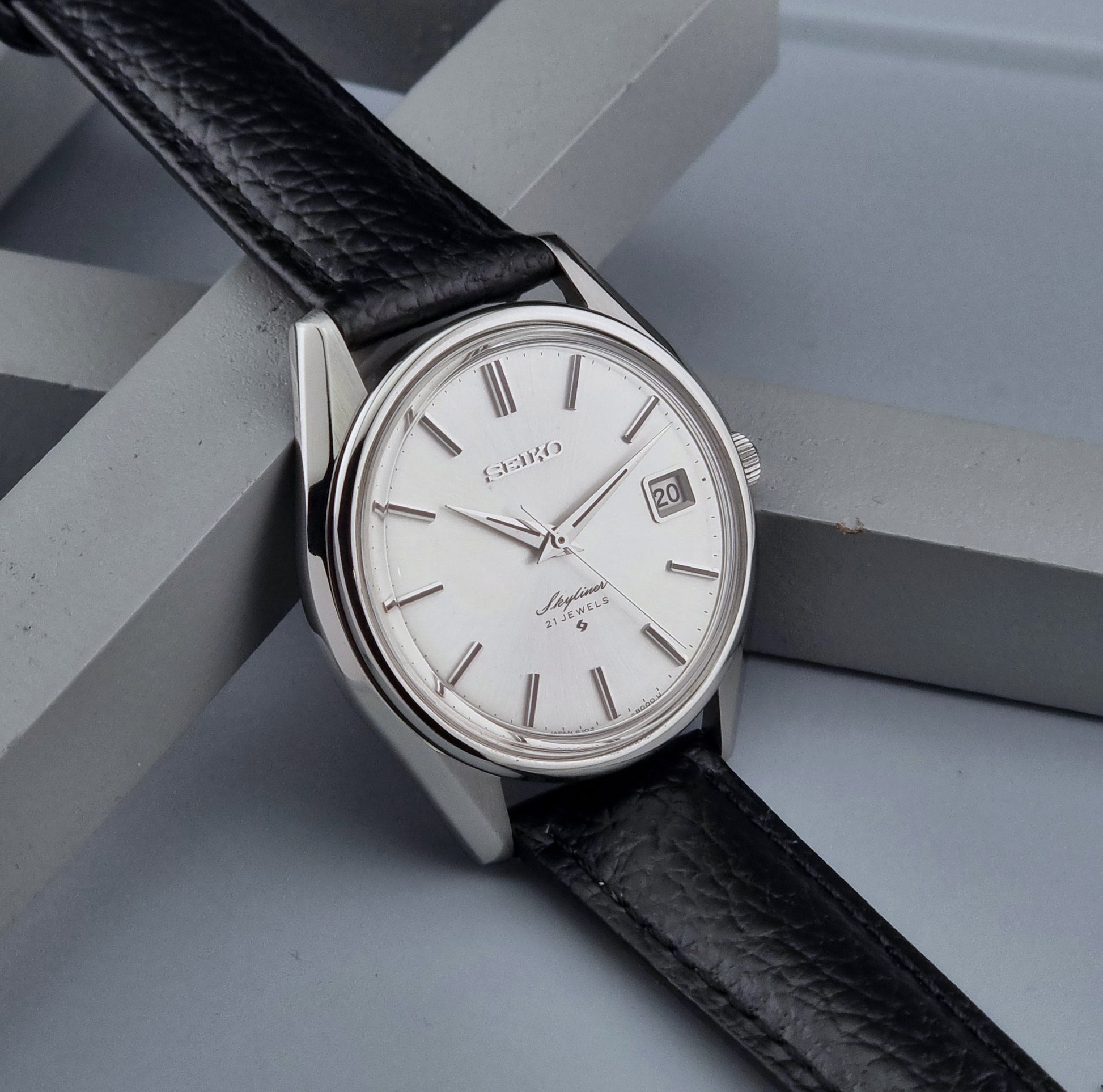 Vintage Seiko Wristwatch Skyliner 6102-8000 with black leather strap and silver case on a light gray background side view