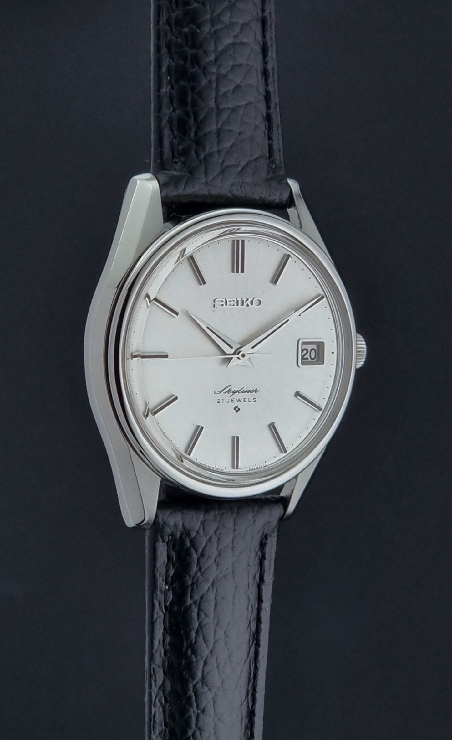 Vintage Seiko Wristwatch Skyliner 6102-8000 with black leather strap and silver case on a light gray background side profile view