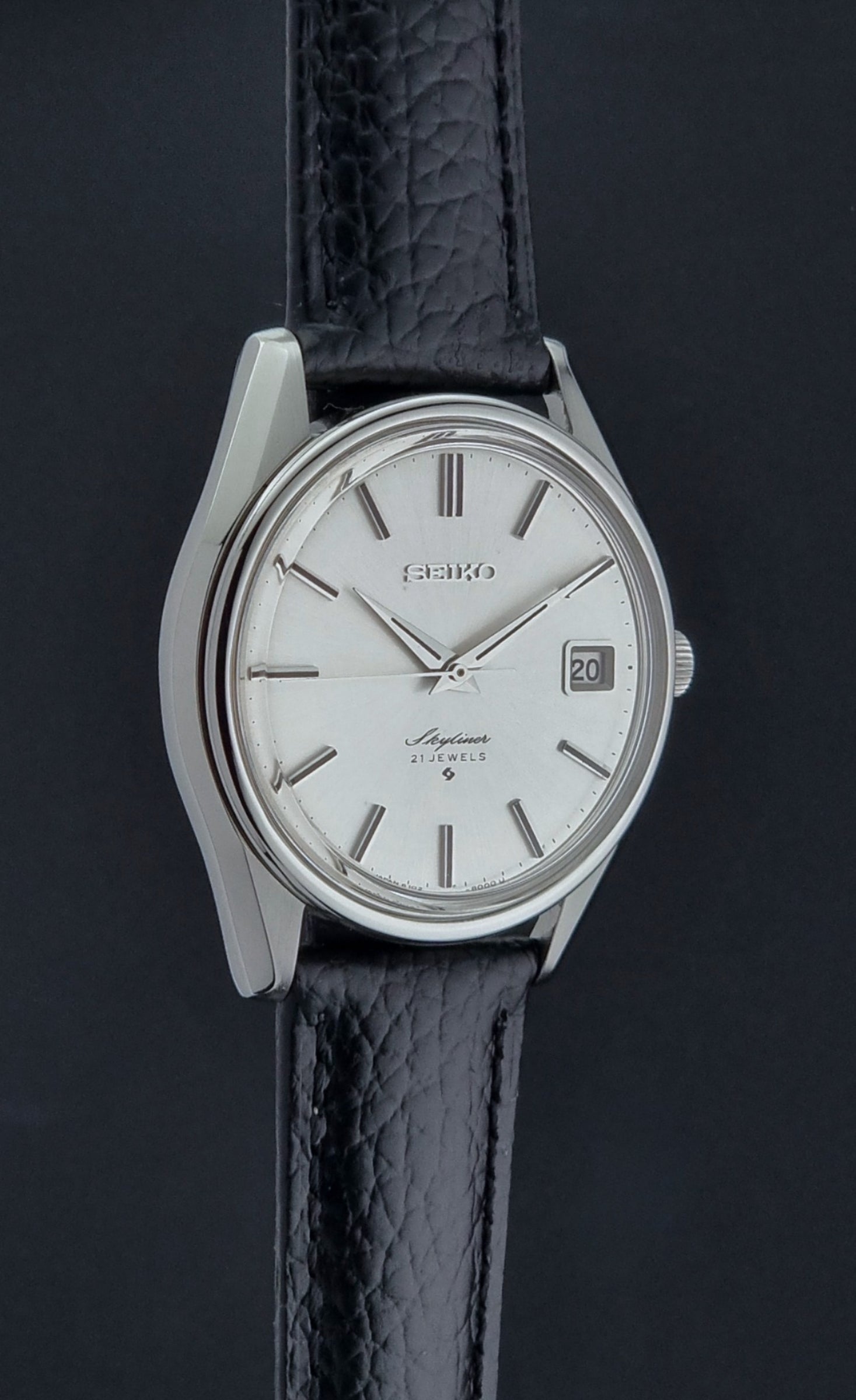 Vintage Seiko Wristwatch Skyliner 6102-8000 with black leather strap and silver case on a light gray background side profile view