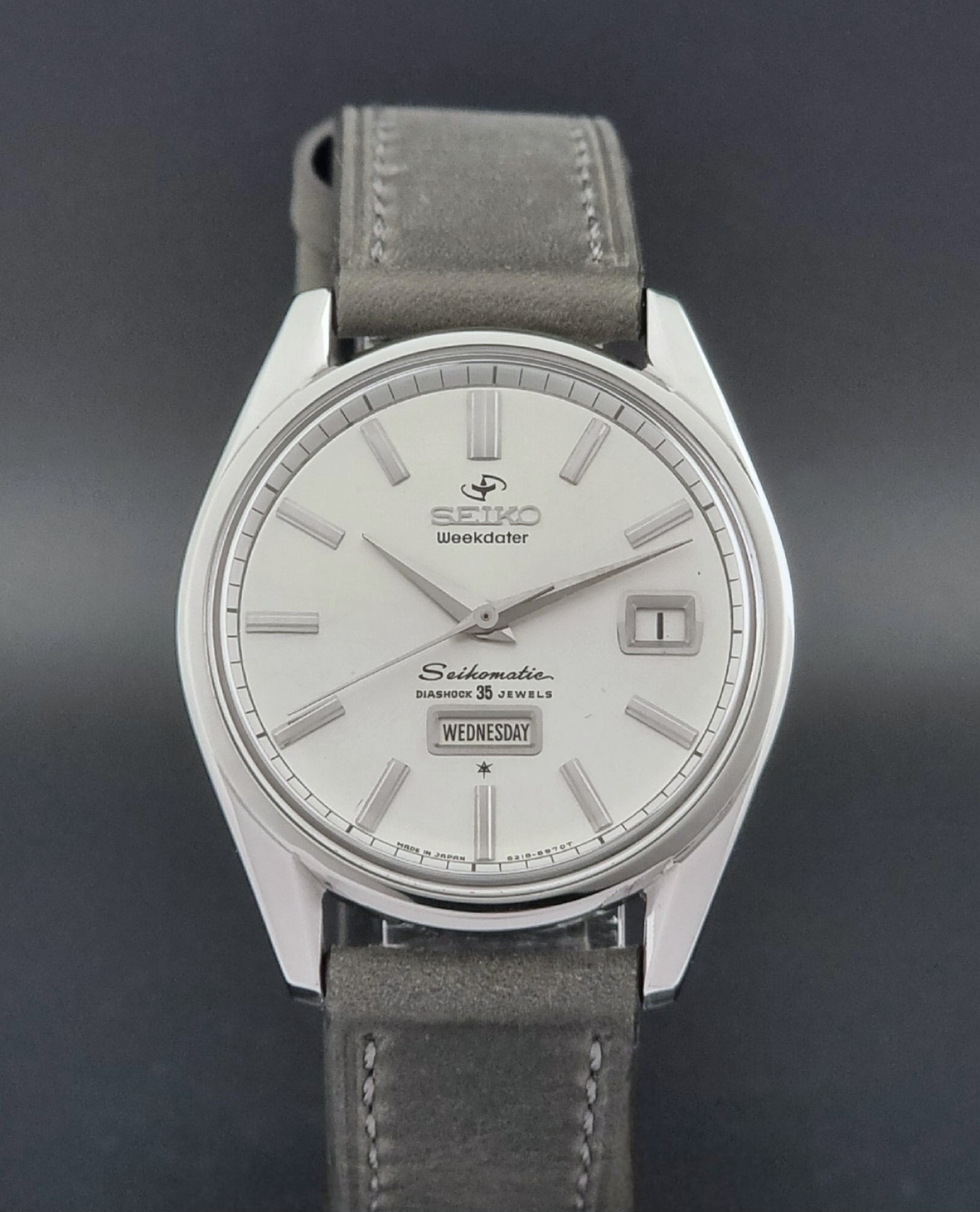 Vintage Seiko watch Seikomatic Weekdater 6218-8970 with a silver case and dark leather strap on a light gray background close dial view