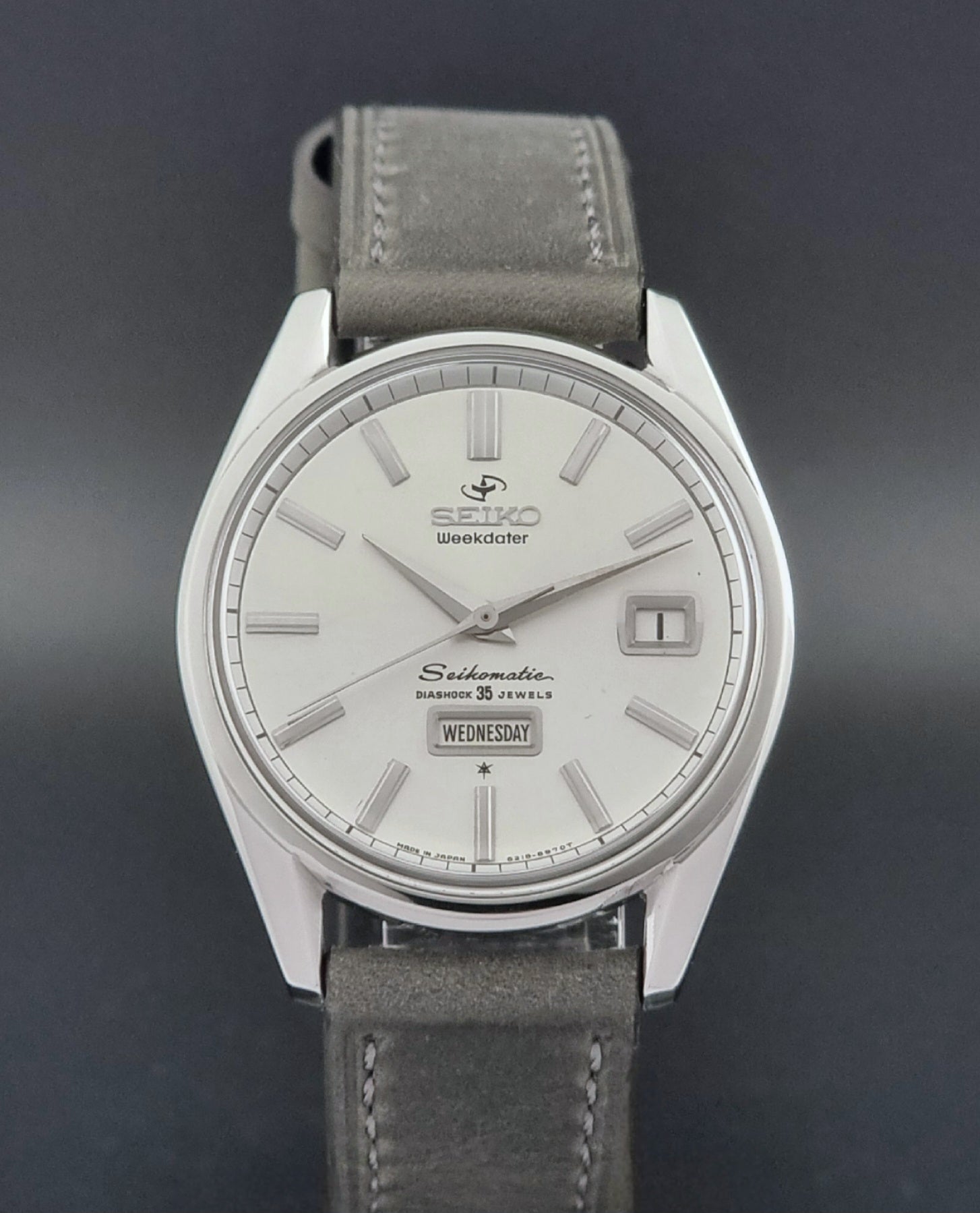 Vintage Seiko watch Seikomatic Weekdater 6218-8970 with a silver case and dark leather strap on a light gray background close dial view
