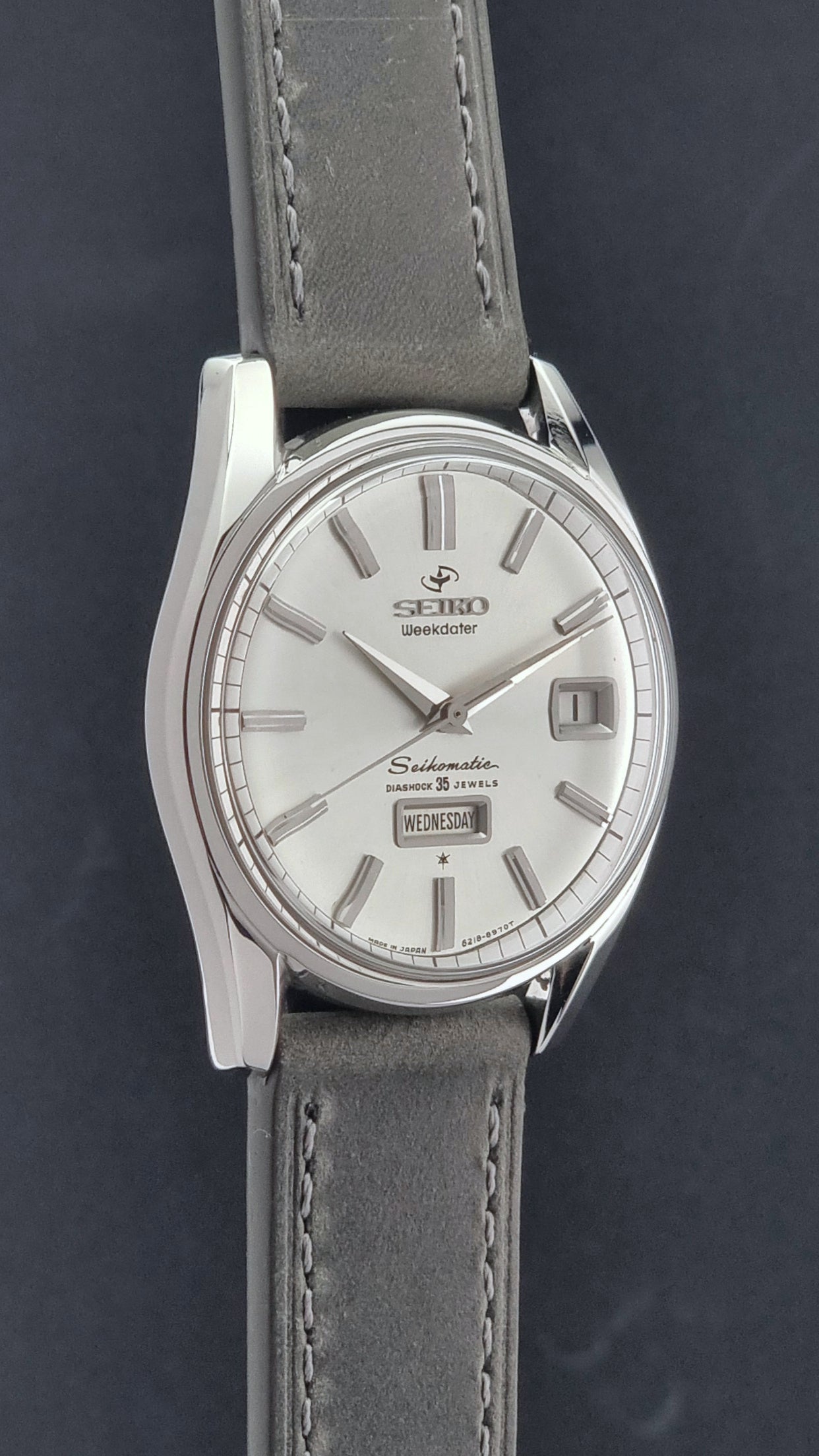 Vintage Seiko watch Seikomatic Weekdater 6218-8970 with a silver case and dark leather strap on a light gray background side profile view