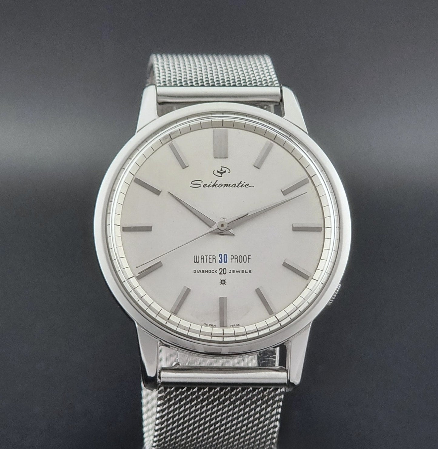 Vintage Seiko Wristwatch Seikomatic J13044E with mesh strap on a dark background close dial view
