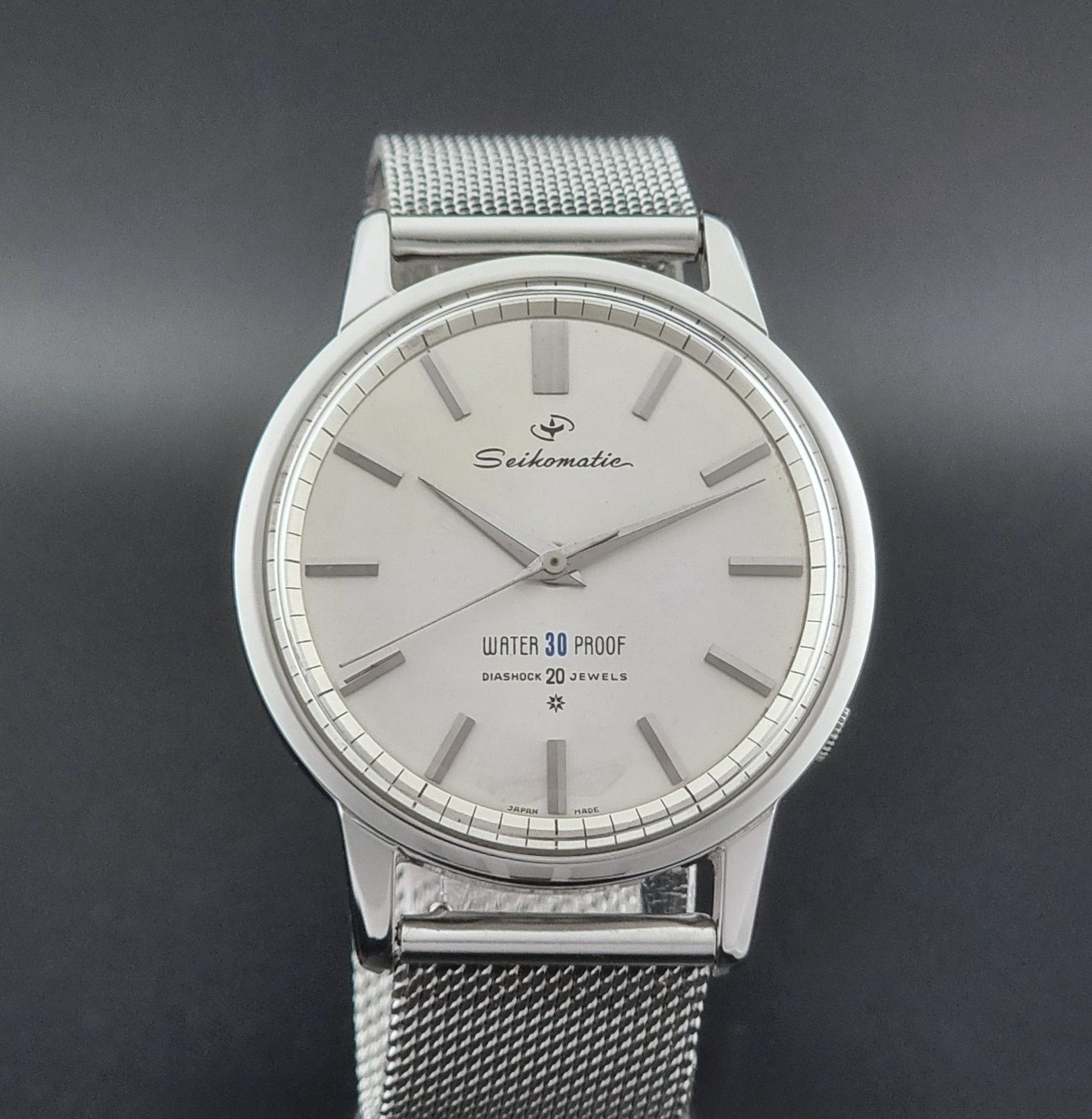 Vintage Seiko Wristwatch Seikomatic J13044E with mesh strap on a dark background close dial view
