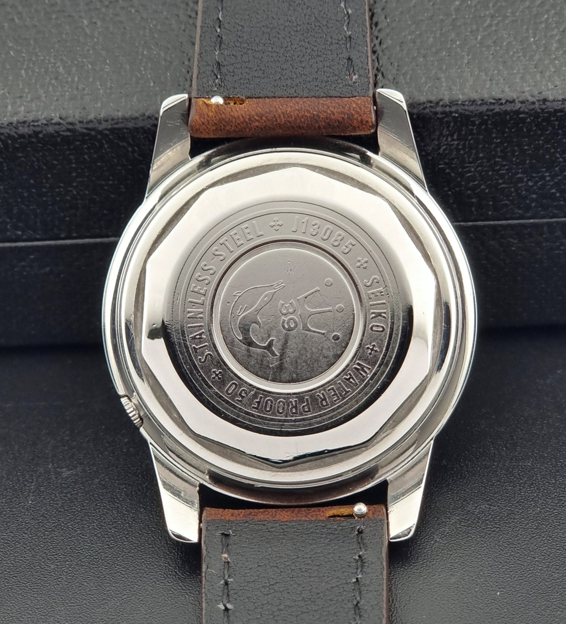 Vintage Seiko Wristwatch Seikomatic J13085 brown leather strap on a dark textured surface case back view