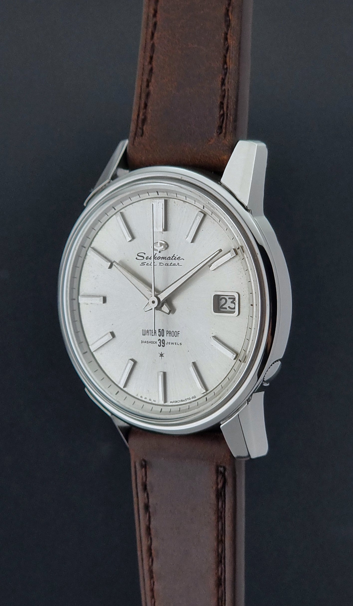Vintage Seiko Wristwatch Seikomatic J13085 brown leather strap on a dark textured surface close crown profile view