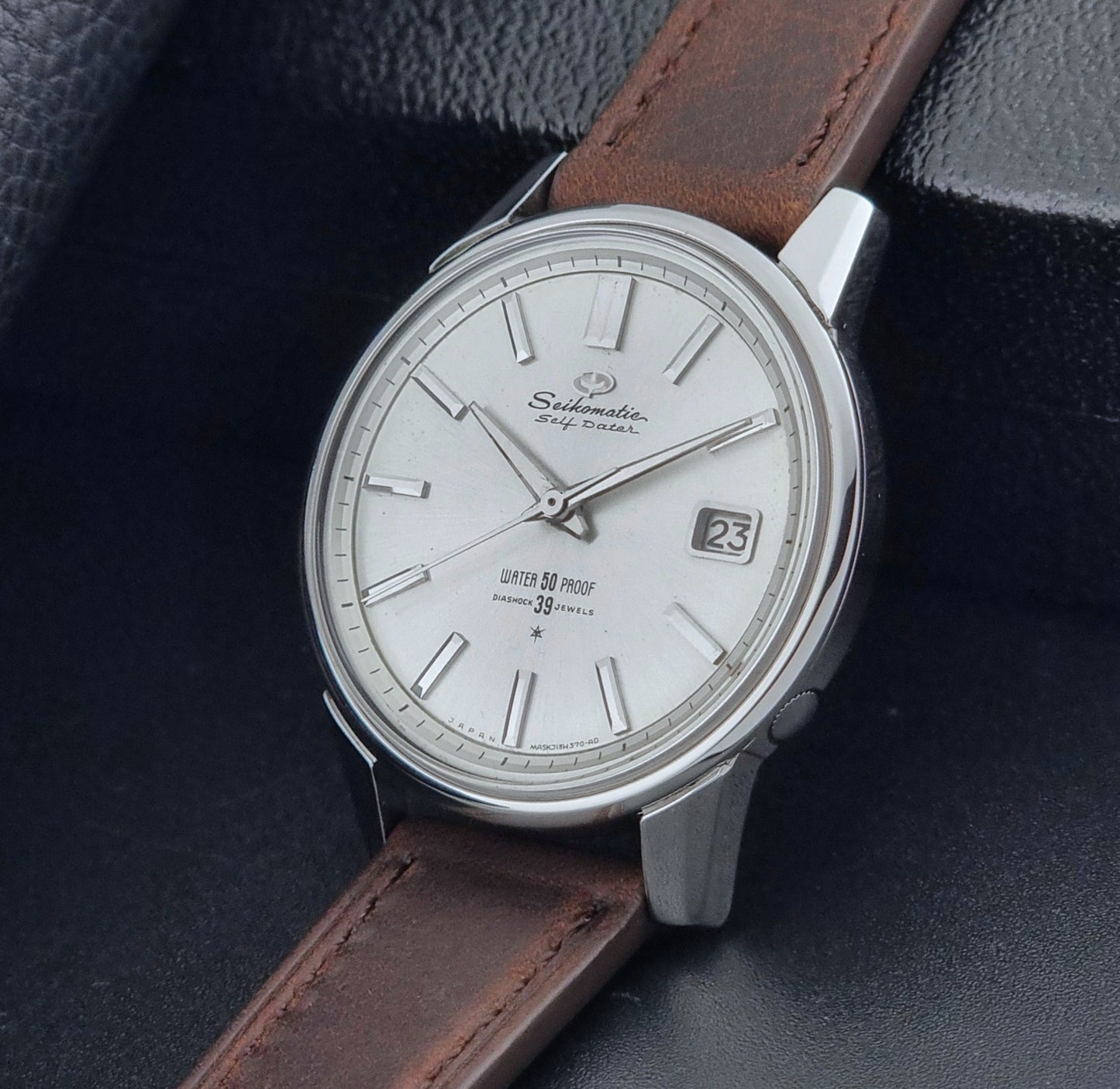 Vintage Seiko Wristwatch Seikomatic J13085 brown leather strap on a dark textured surface crown view