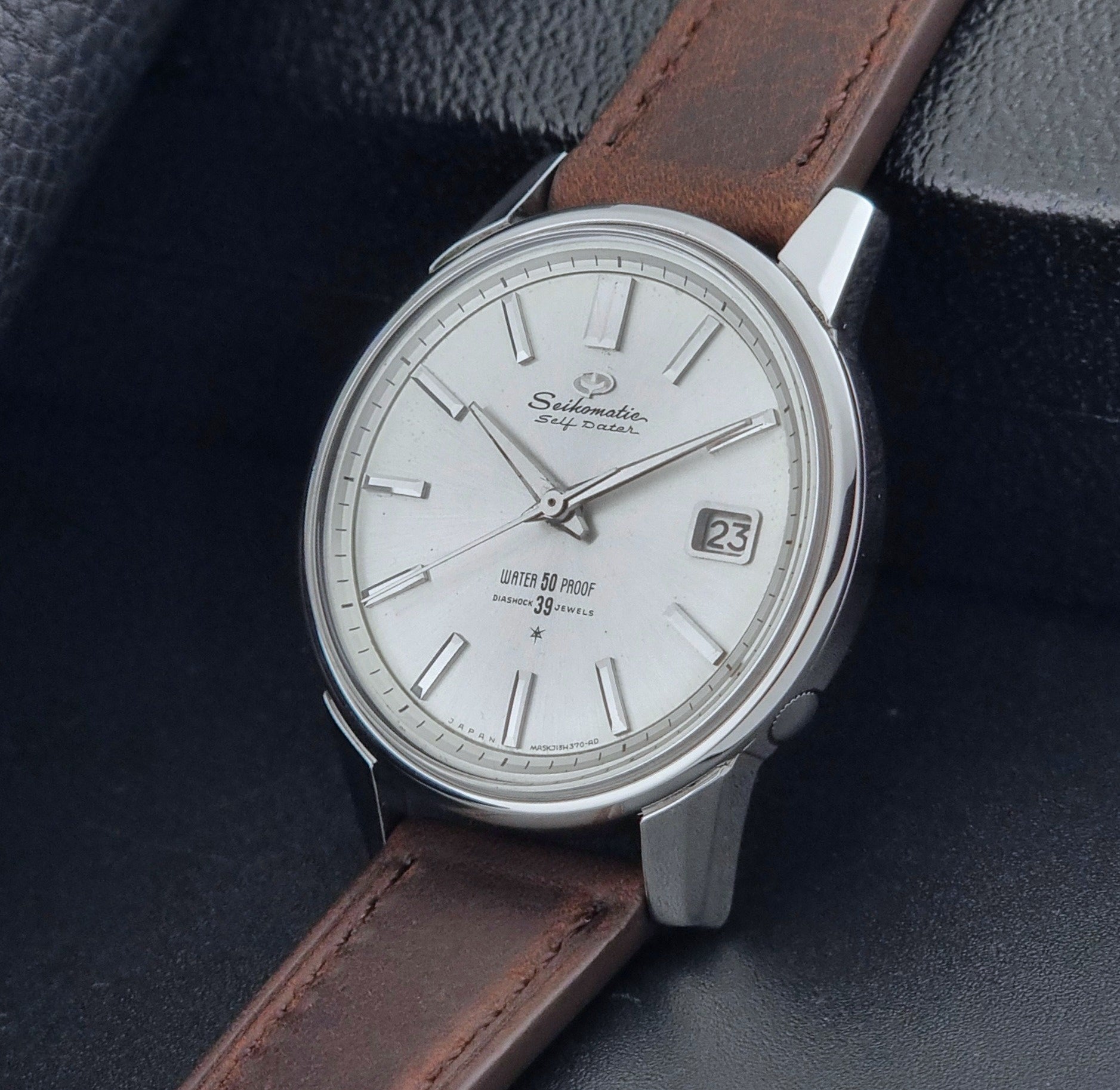 Vintage Seiko Wristwatch Seikomatic J13085 brown leather strap on a dark textured surface crown view