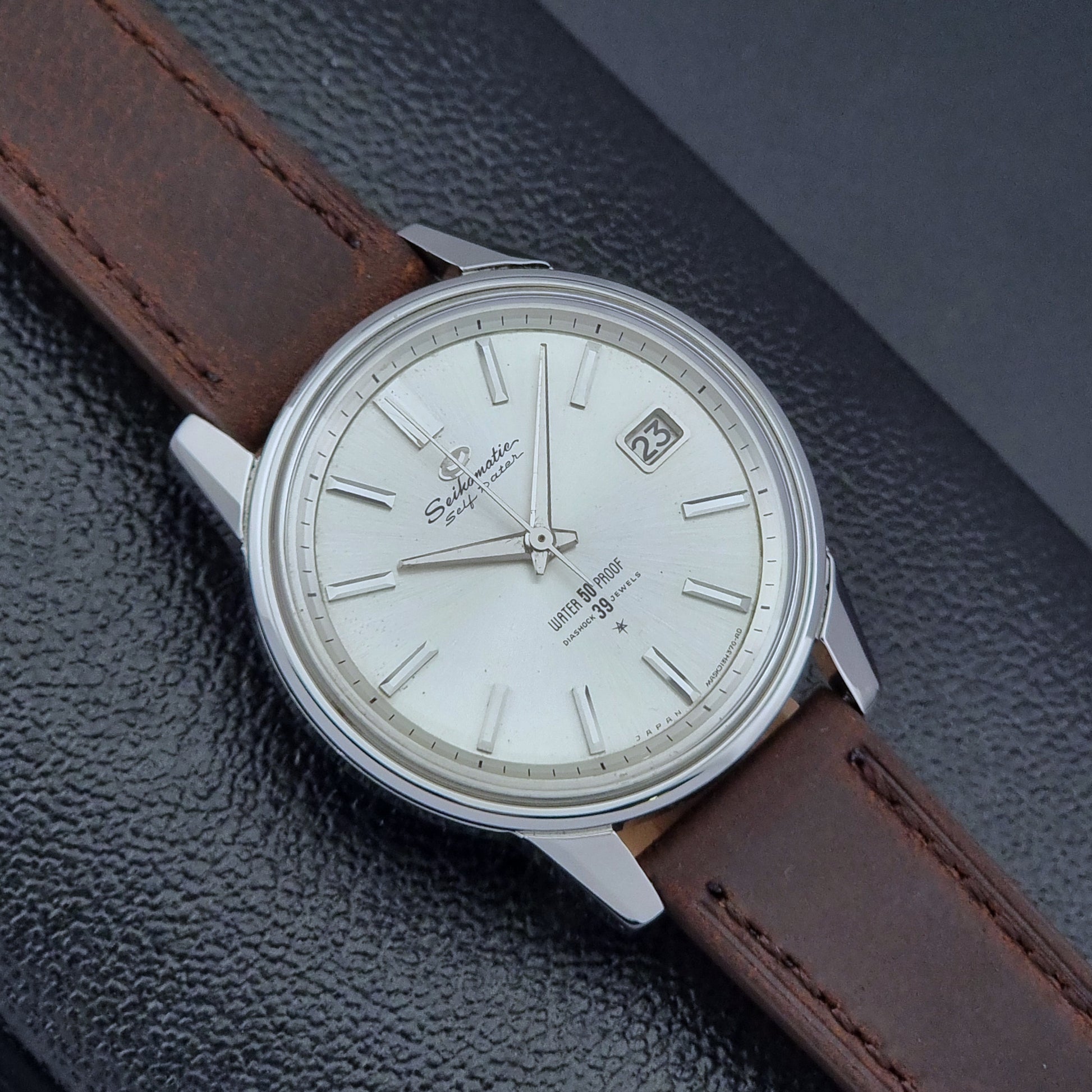 Vintage Seiko Wristwatch Seikomatic J13085 brown leather strap on a dark textured surface dial view