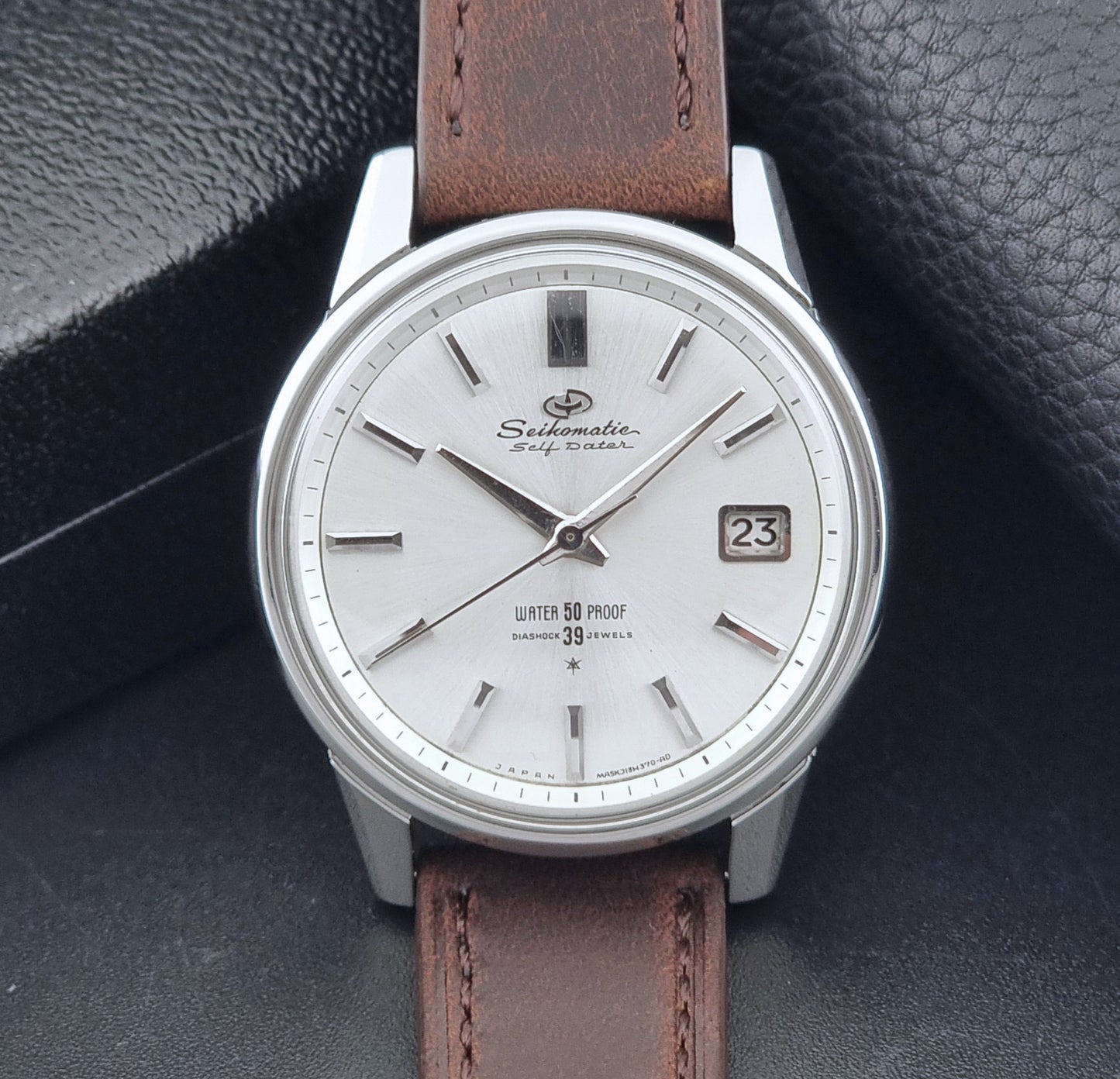 Vintage Seiko Wristwatch Seikomatic J13085 brown leather strap on a dark textured surface front view