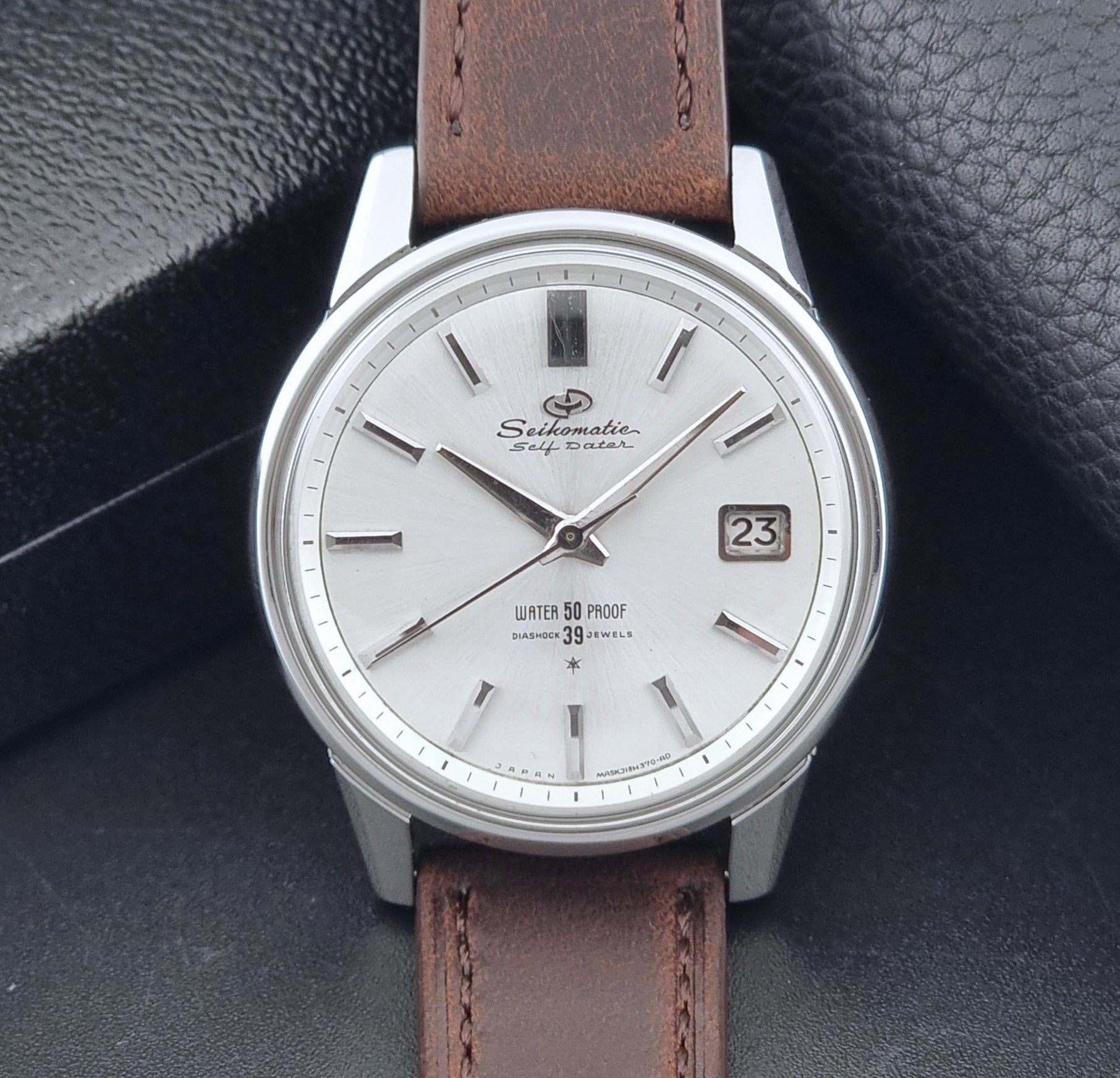 Vintage Seiko Wristwatch Seikomatic J13085 brown leather strap on a dark textured surface front view
