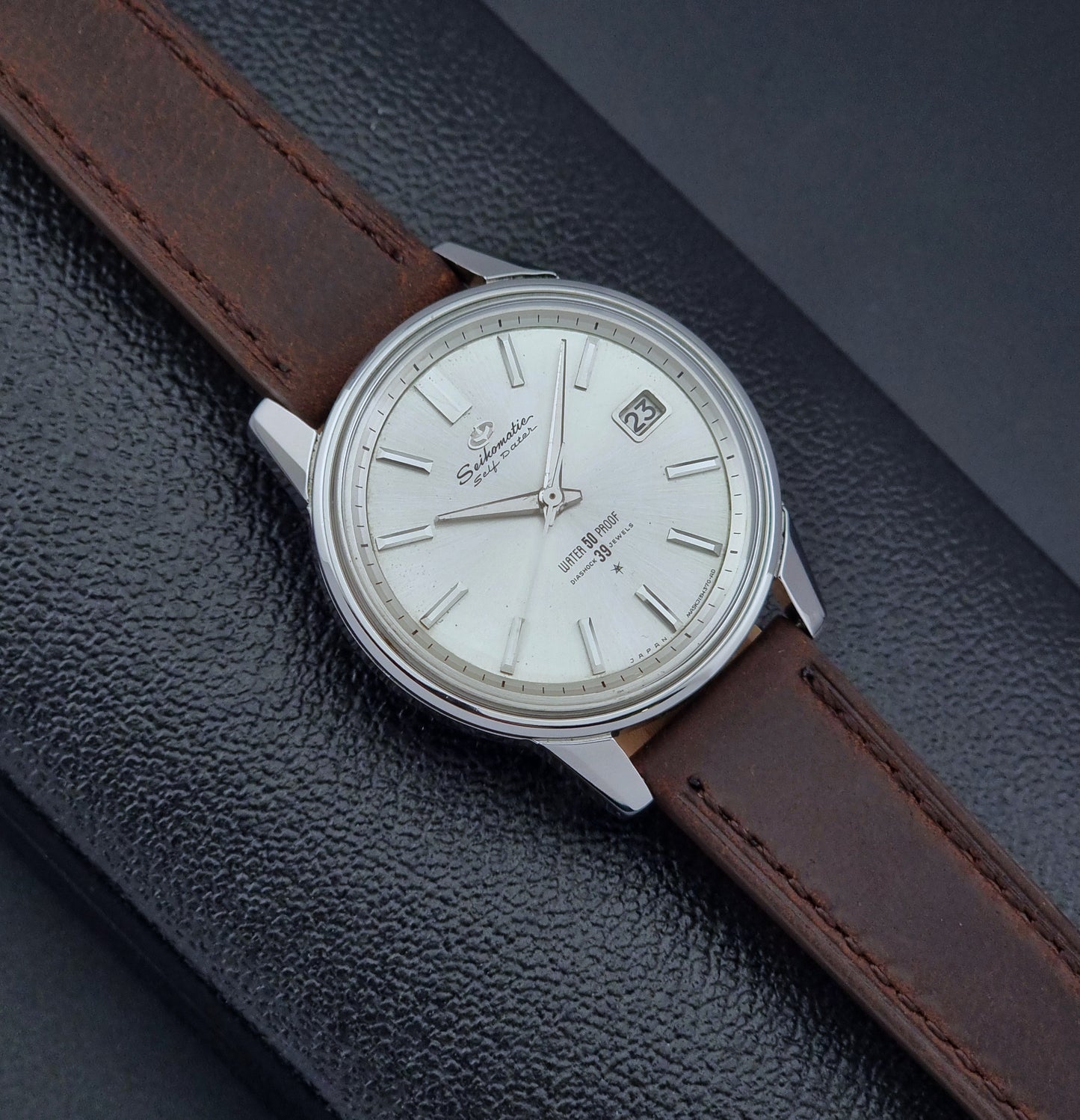 Vintage Seiko Wristwatch Seikomatic J13085 brown leather strap on a dark textured surface front