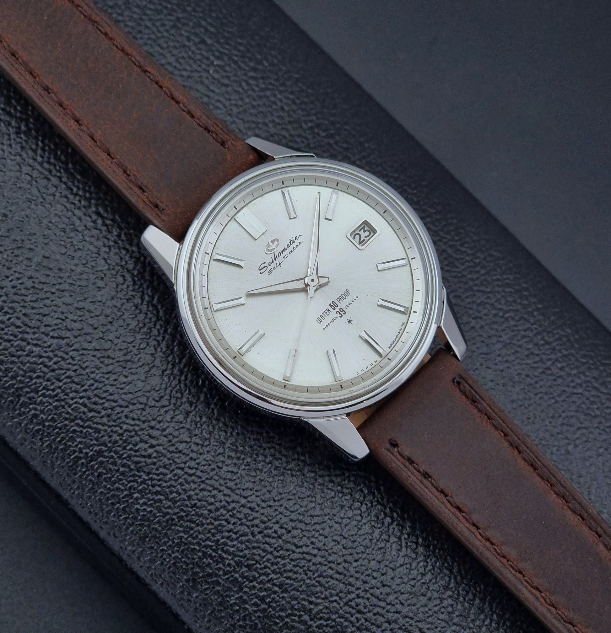 Vintage Seiko Wristwatch Seikomatic J13085 brown leather strap on a dark textured surface front