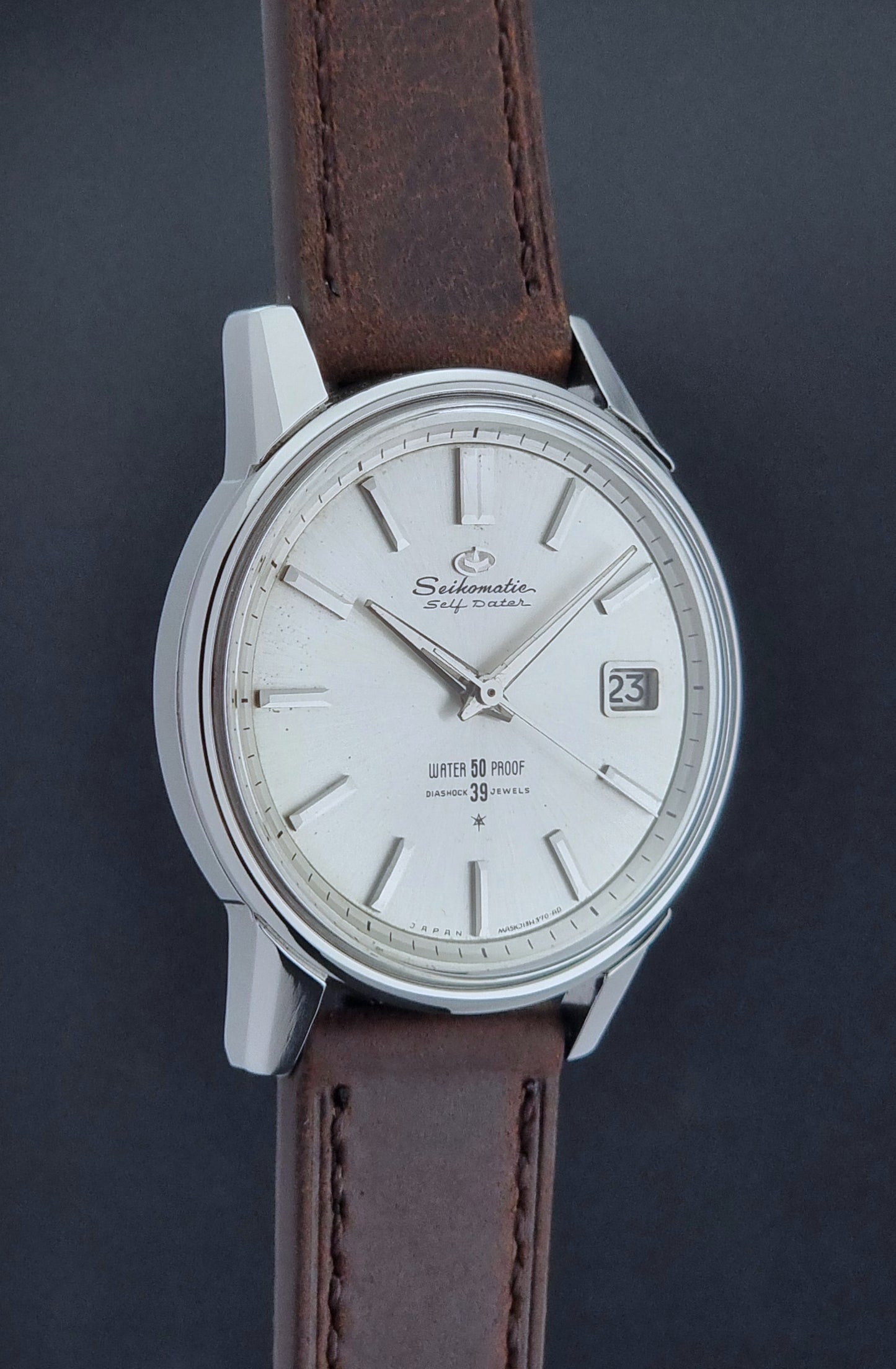 Vintage Seiko Wristwatch Seikomatic J13085 brown leather strap on a dark textured surface close side profile view