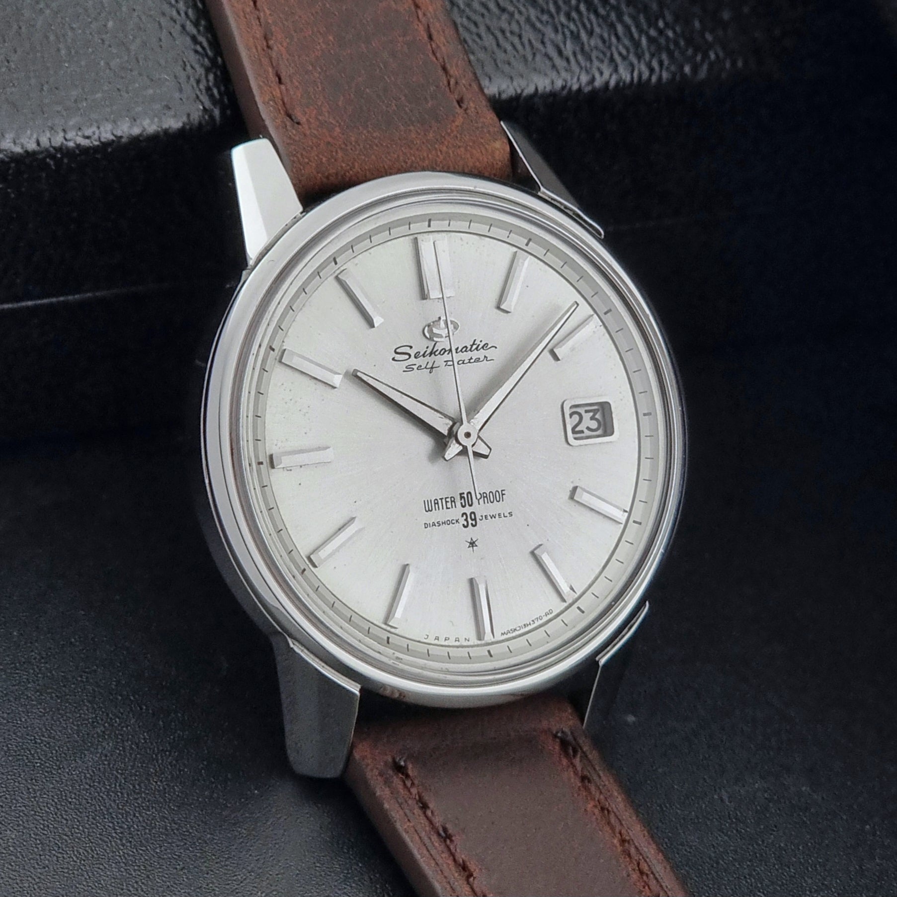 Vintage Seiko Wristwatch Seikomatic J13085 brown leather strap on a dark textured surface side view