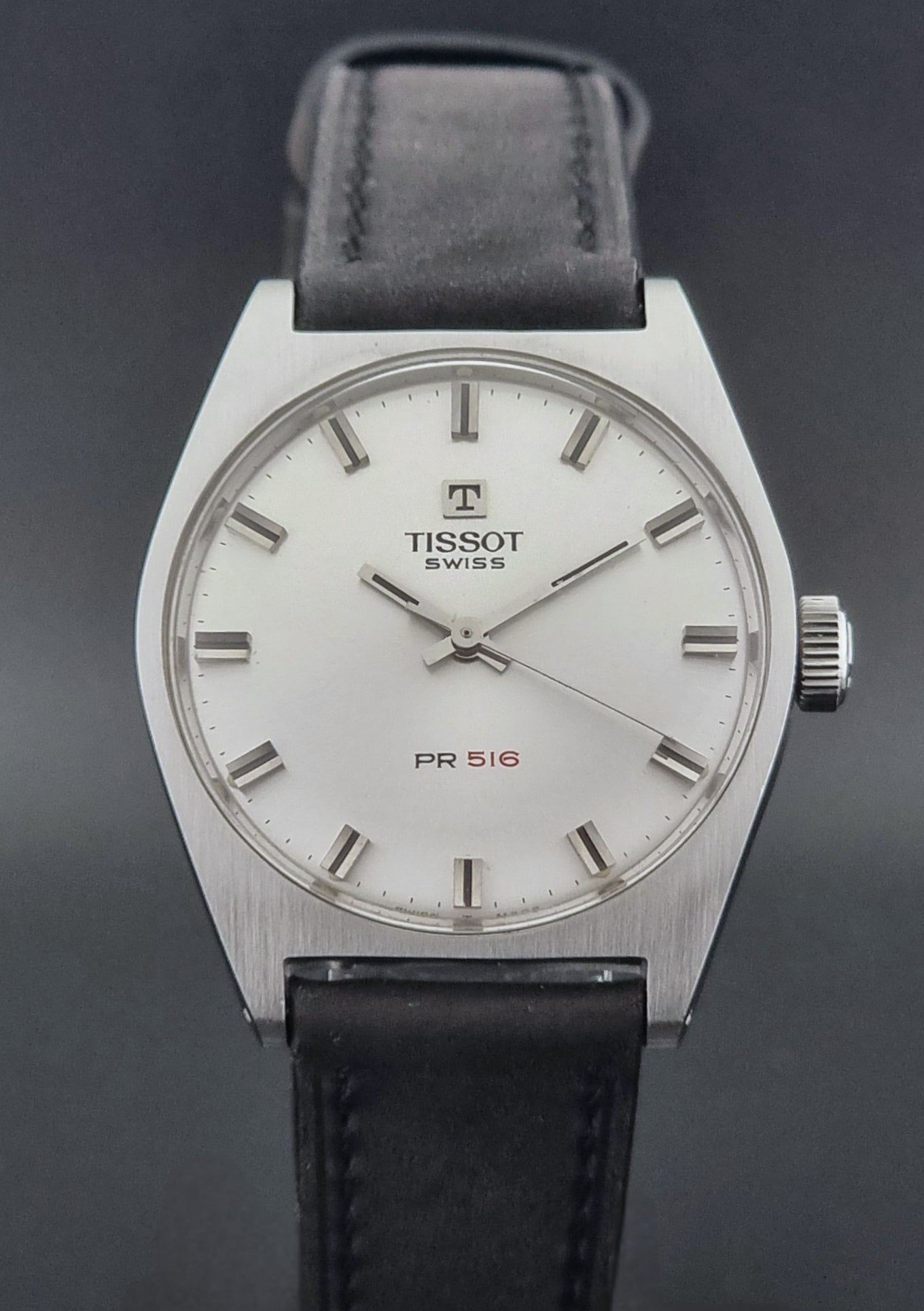 Vintage Tissot Wristwatch 41620 PR 516 with black leather strap on a grey surface close dial view