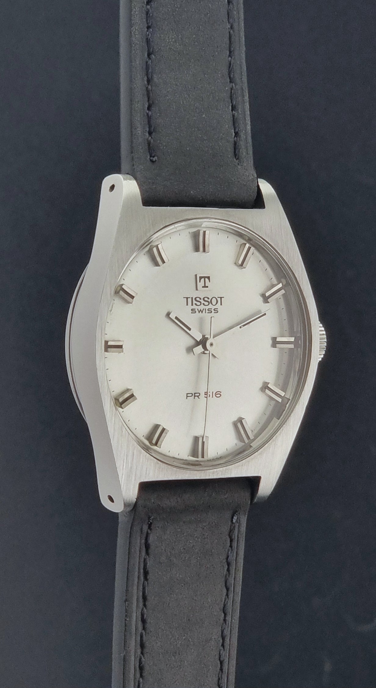 Vintage Tissot Wristwatch 41620 PR 516 with black leather strap on a grey surface side profile view