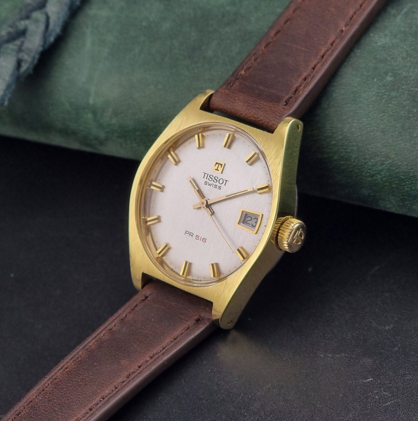 Vintage Tissot Watch 41620 PR 516 in Gold with brown leather strap on a green background crown view
