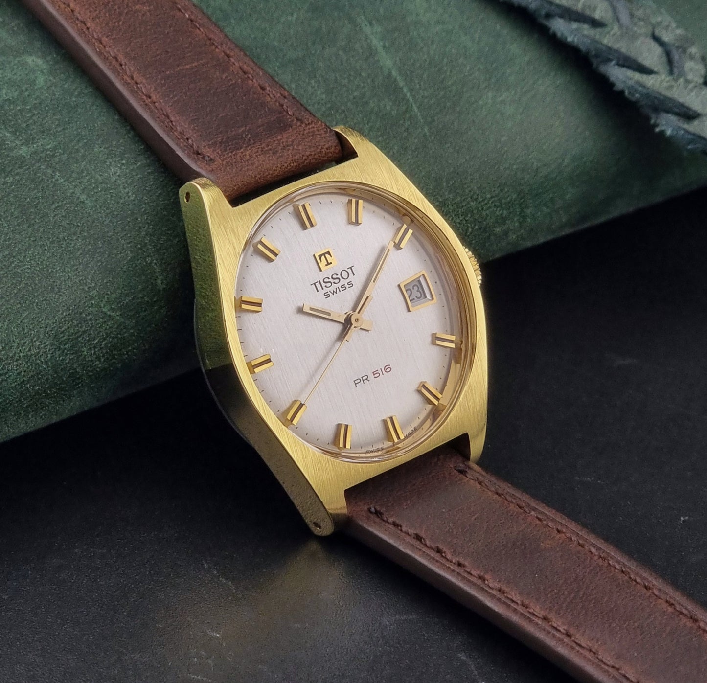 Vintage Tissot Watch 41620 PR 516 in Gold with brown leather strap on a green background side view