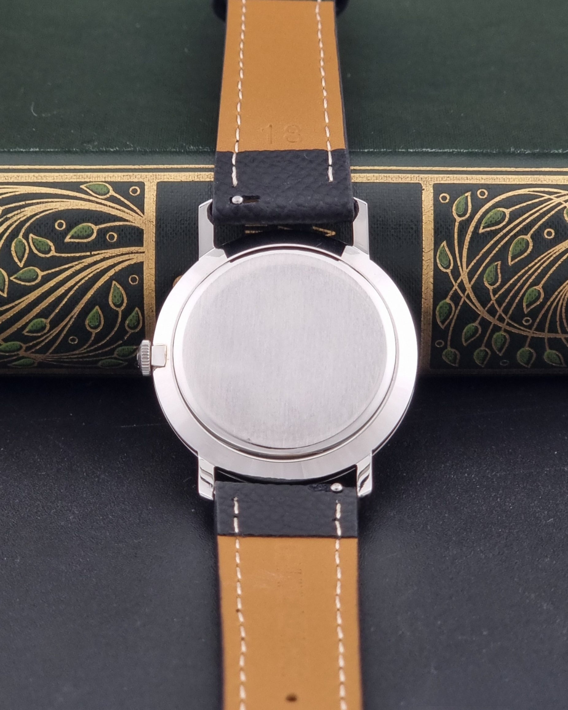 Vintage Tudor 9800 watch with black leather strap on a dark gray background case back view