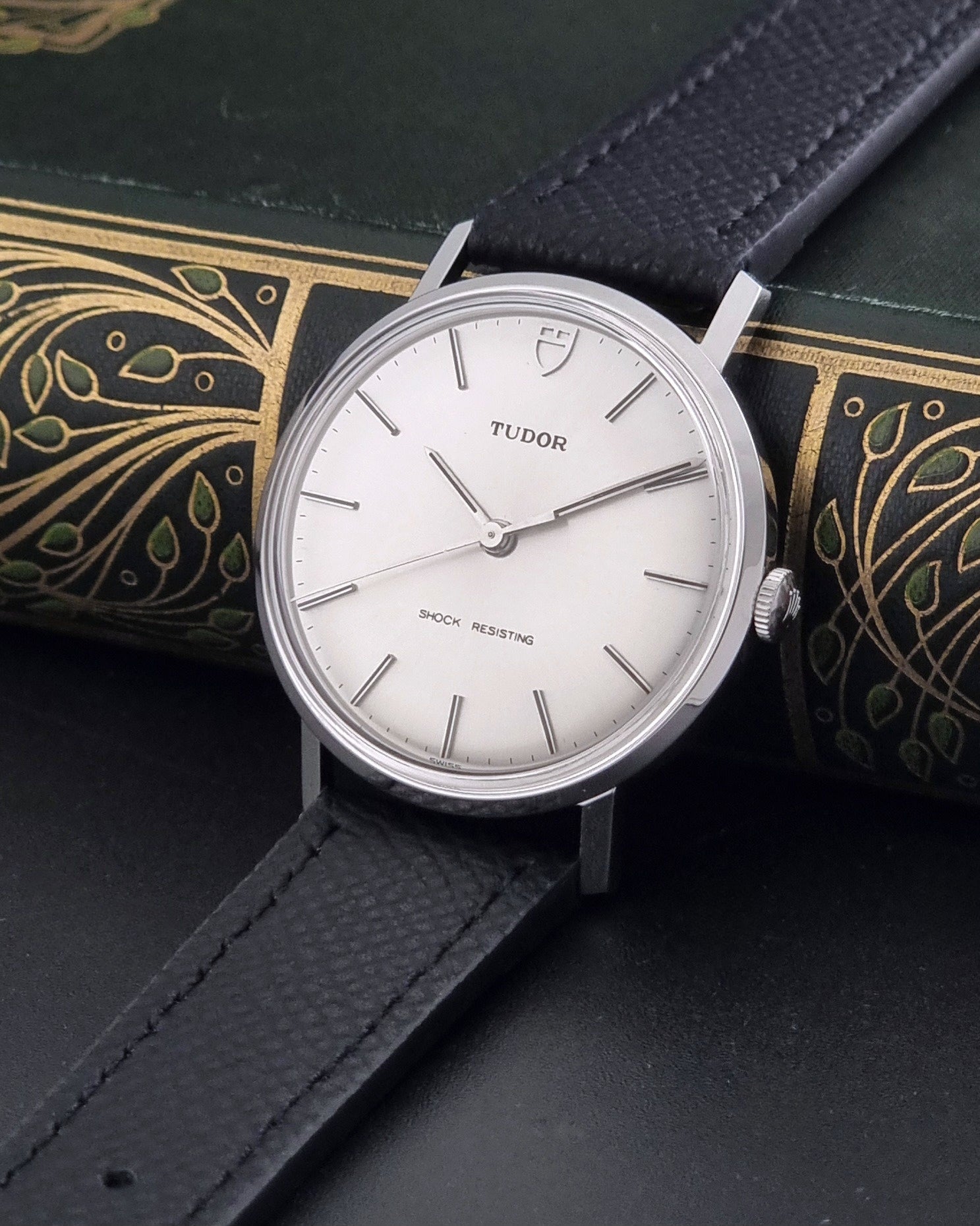 Vintage Tudor 9800 watch with black leather strap on a dark gray background crown view