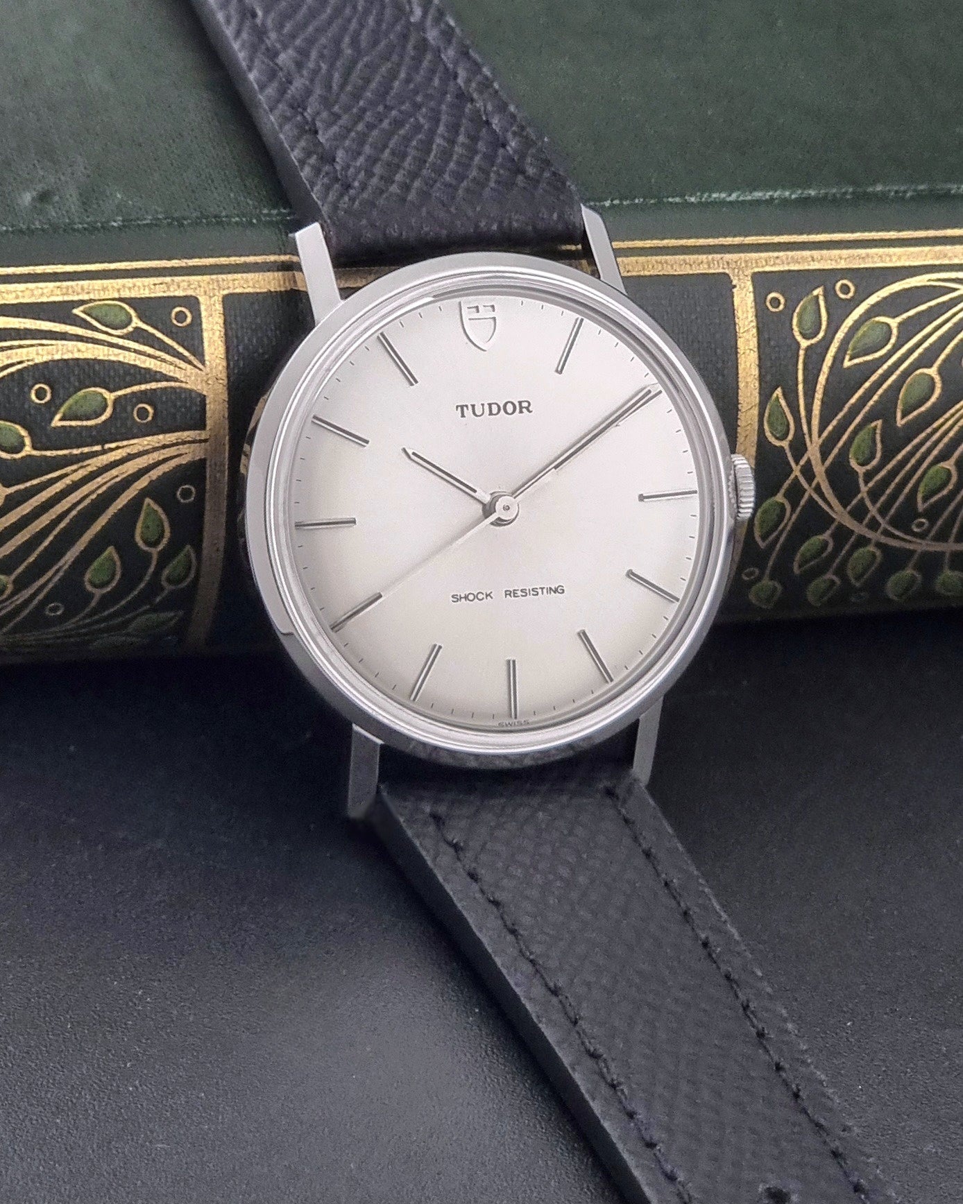 Vintage Tudor 9800 watch with black leather strap on a dark gray background side view