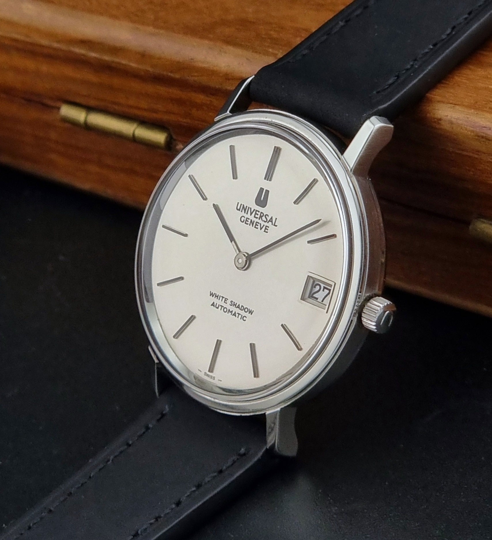 Universal Geneve Watch with black strap and white dial on a wooden surface