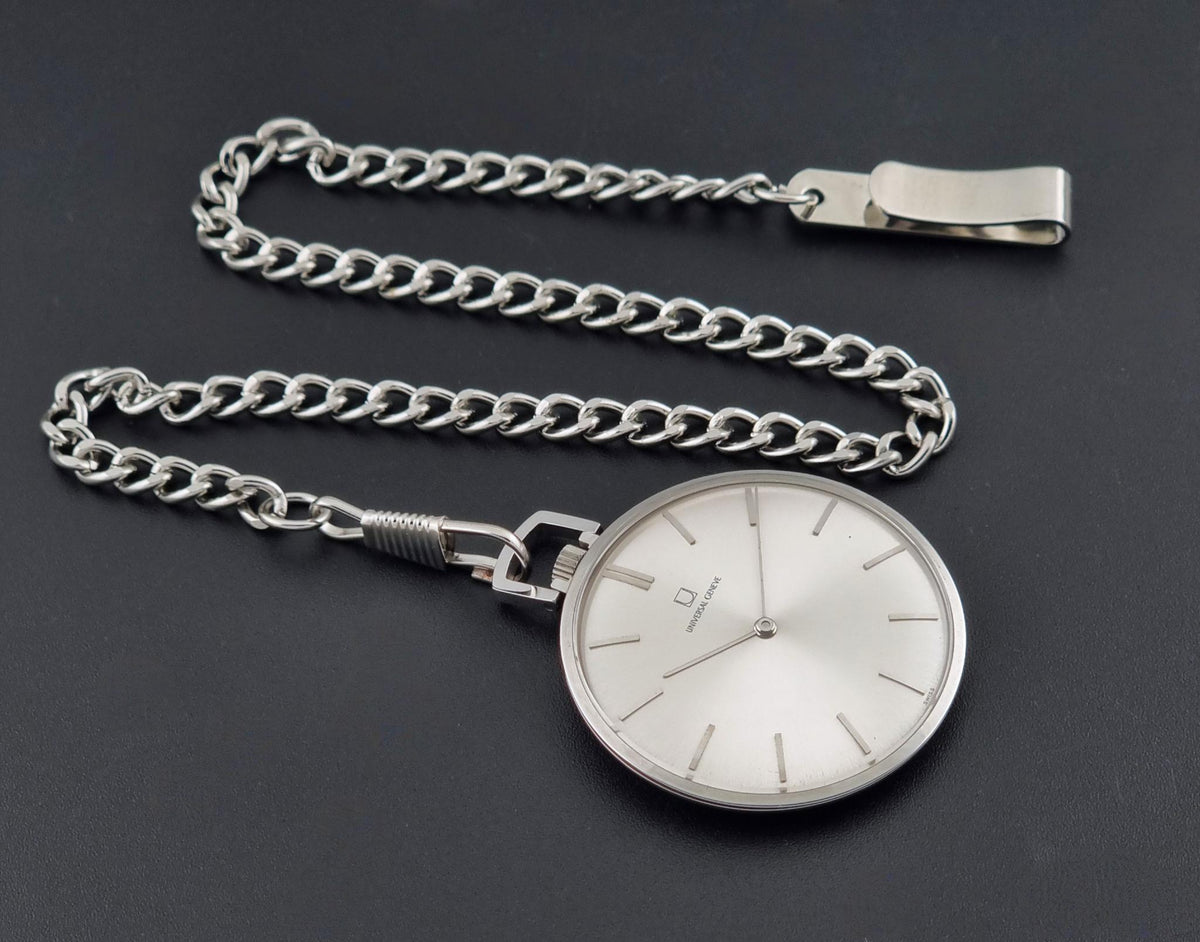A Vintage Universal Geneve 856105/01 Pocket Watch silver-tone pocket watch with a matching curb chain and clip, displayed on a dark gray background.