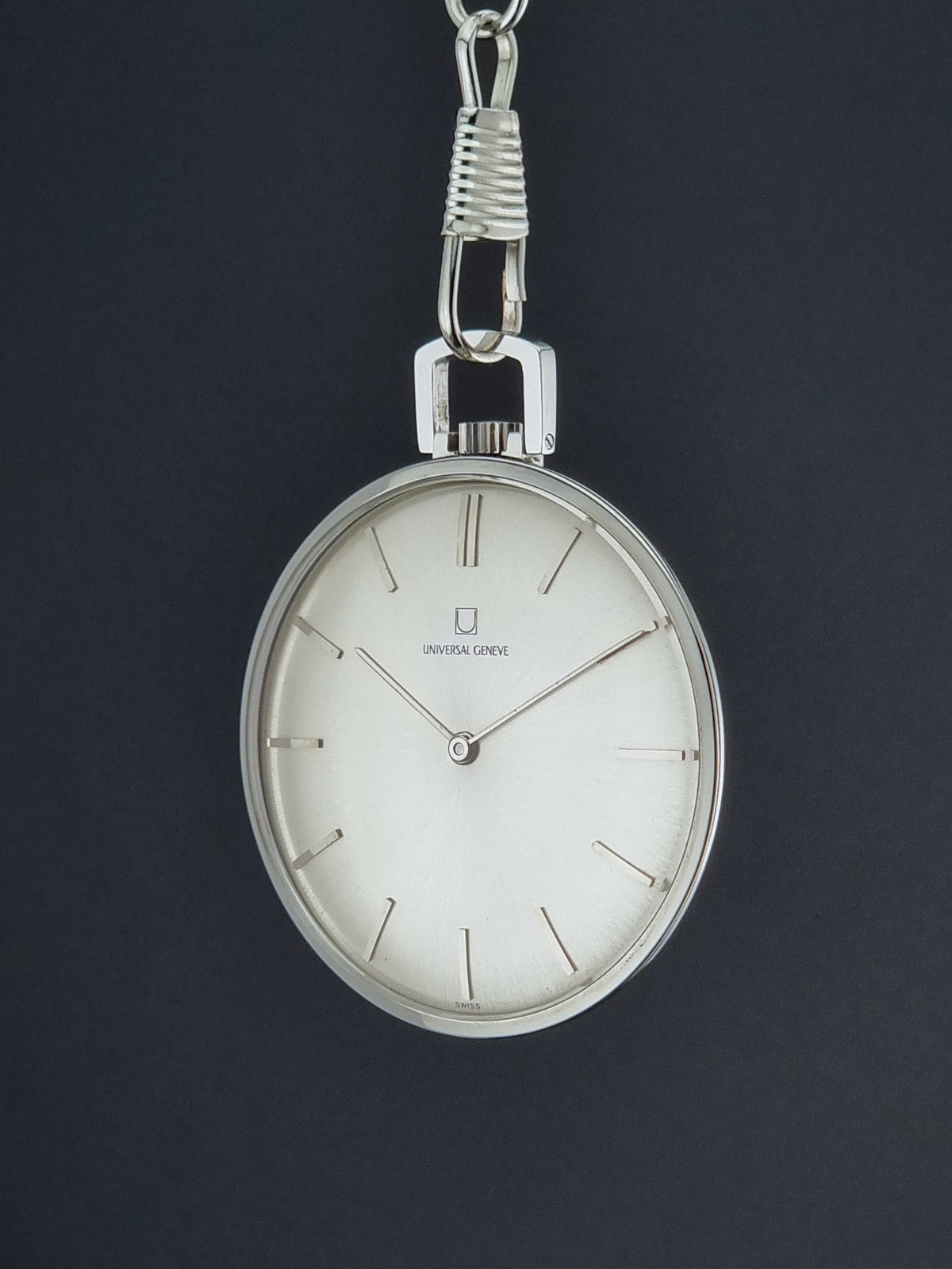 A Universal Geneve 856105/01 vintage-style silver pocket watch with a white dial and minimalist hour markers, hanging against a dark black background.
