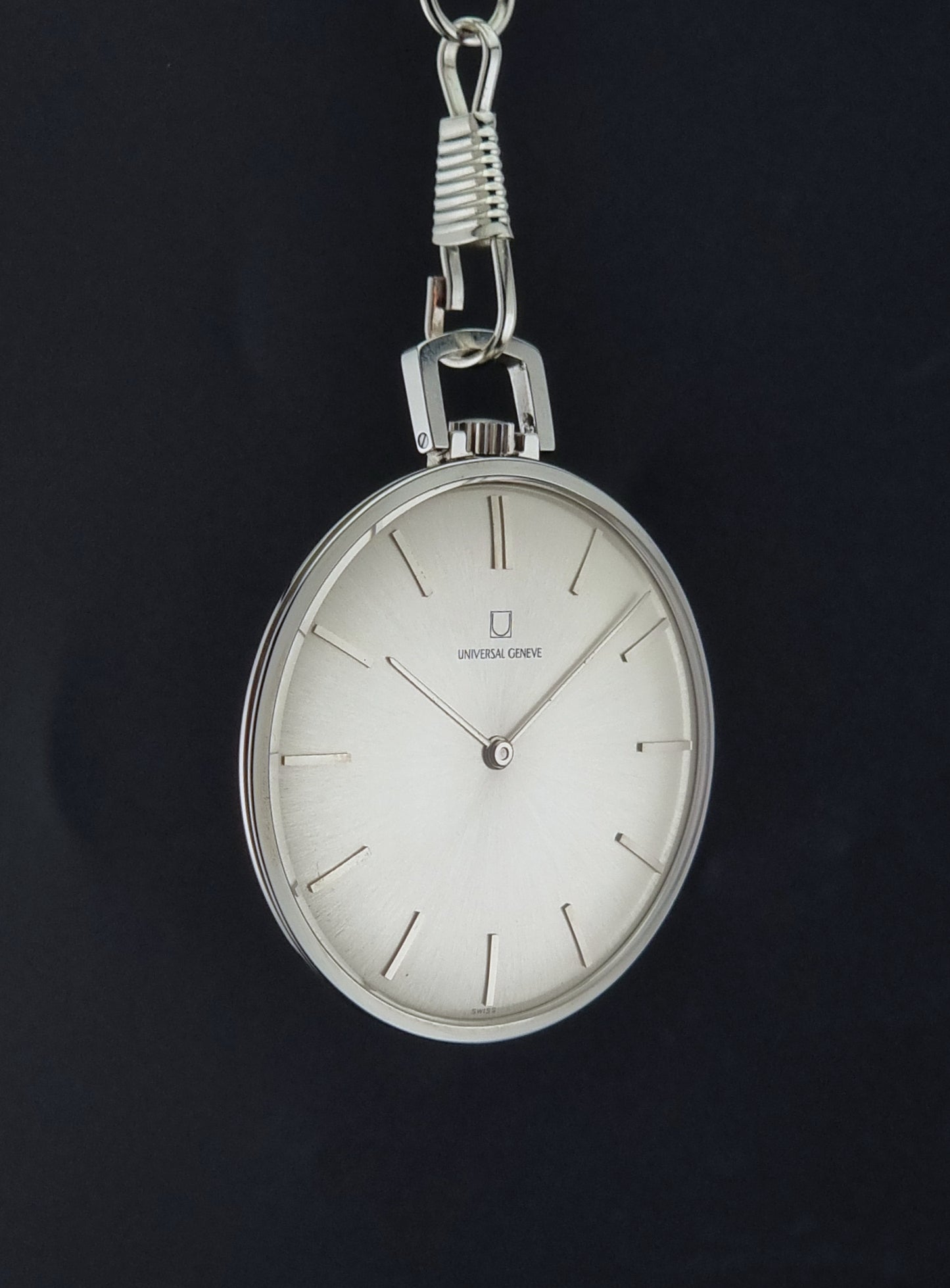 A Universal Geneve 856105/01 Pocket Watch vintage-style silver pocket watch with a white dial and minimalist hour markers, hanging against a dark black background.