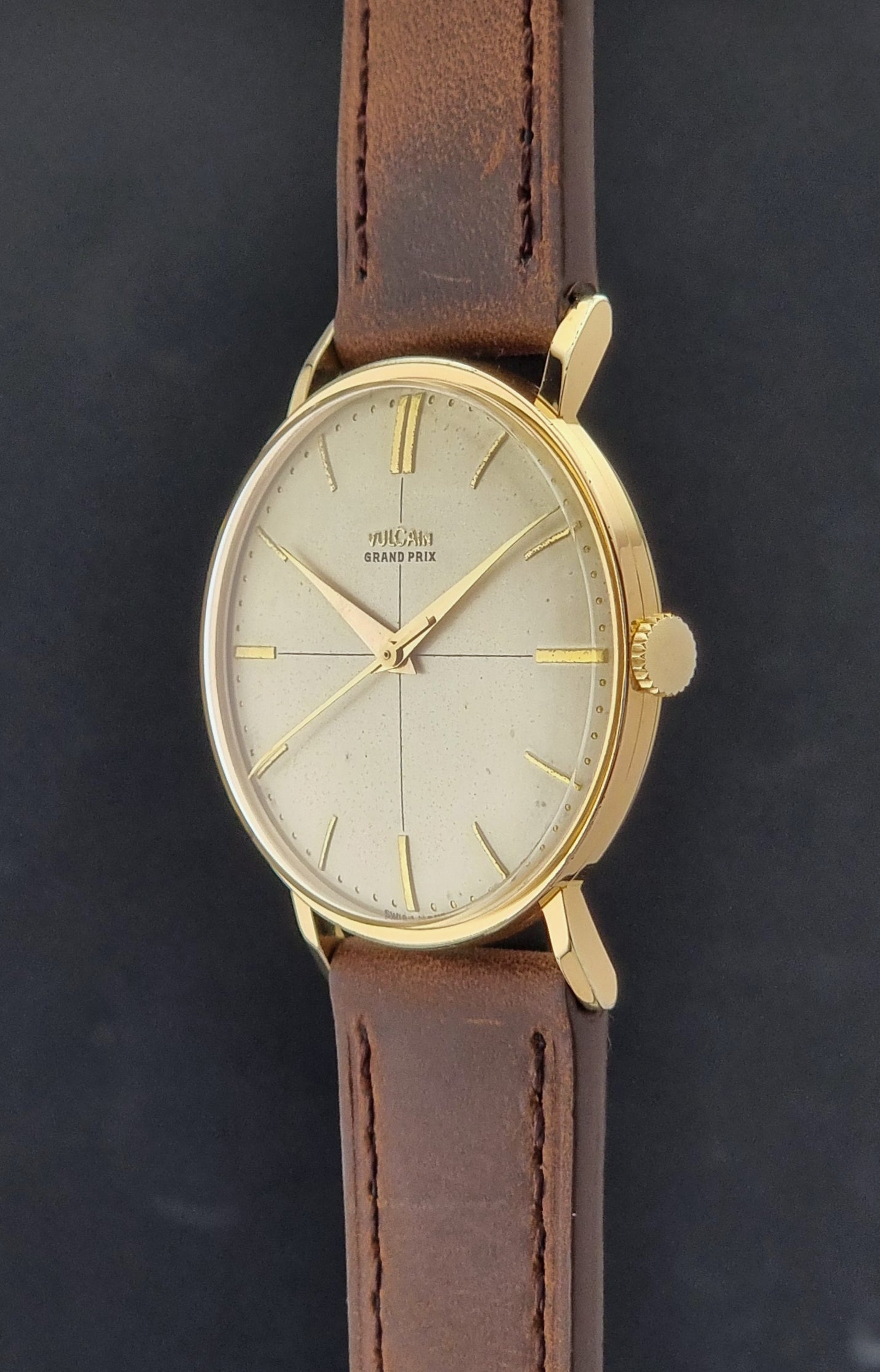 Vintage Vulcain Grand Prix watch with brown leather strap and gold case on a dark surface crown profile view