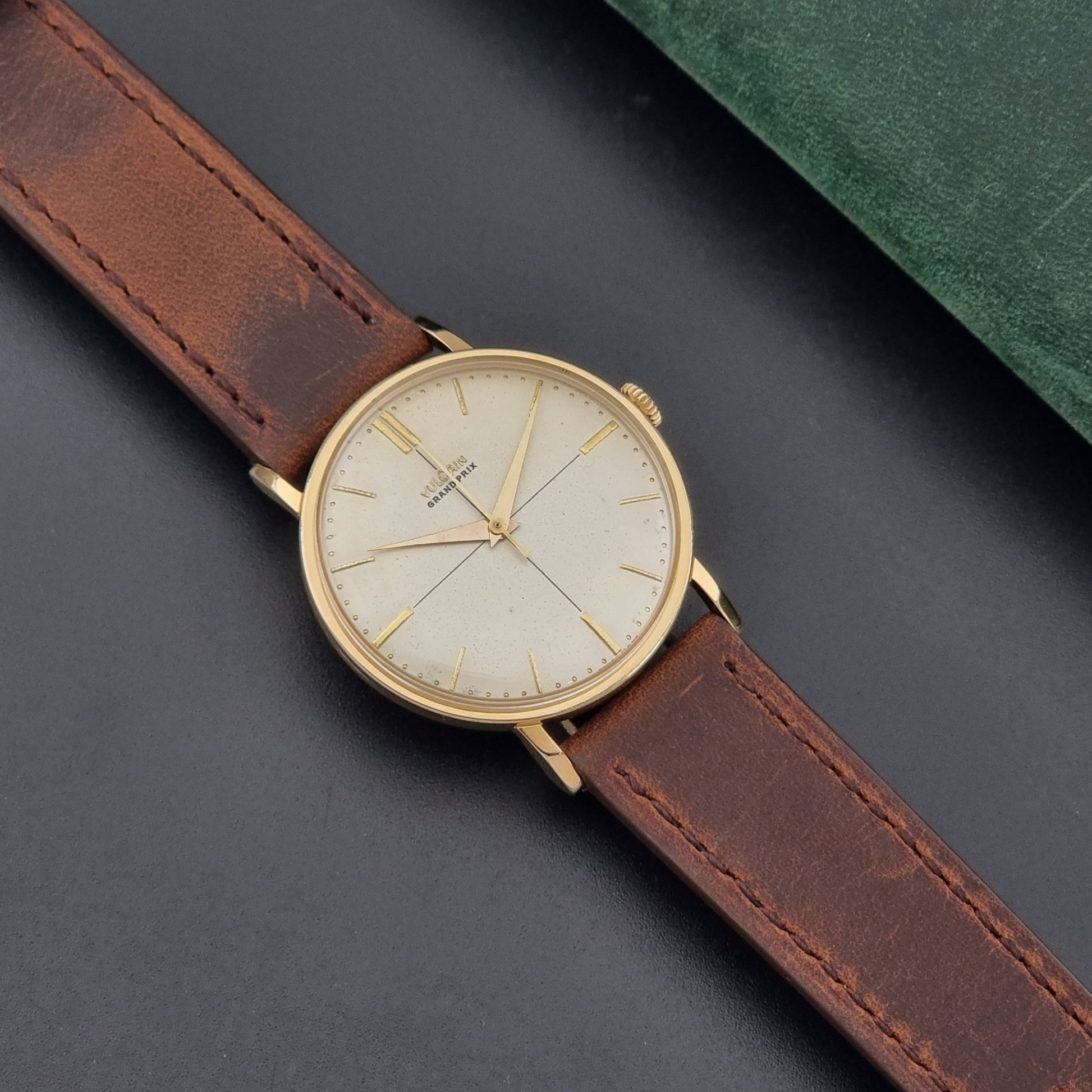 Vintage Vulcain Grand Prix watch with brown leather strap and gold case on a dark surface dial