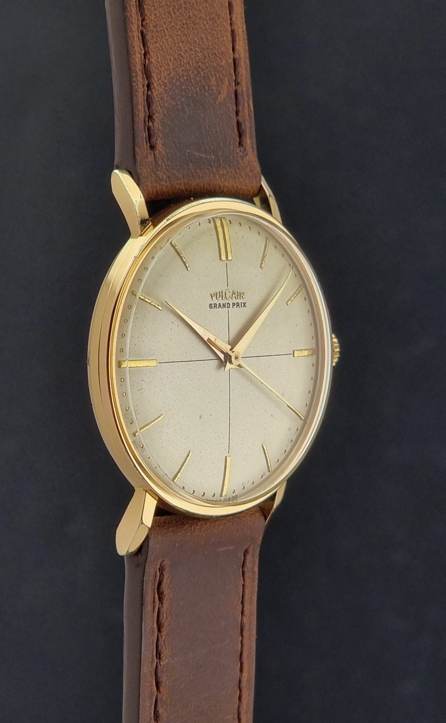 Vintage Vulcain Grand Prix watch with brown leather strap and gold case on a dark surface side profile view