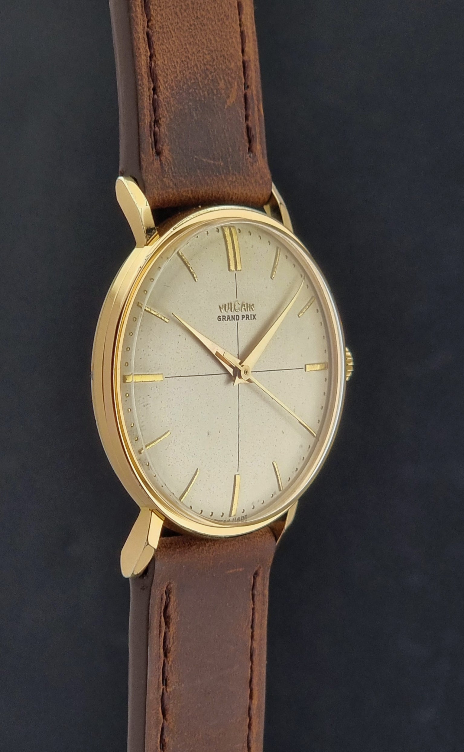 Vintage Vulcain Grand Prix watch with brown leather strap and gold case on a dark surface side profile view